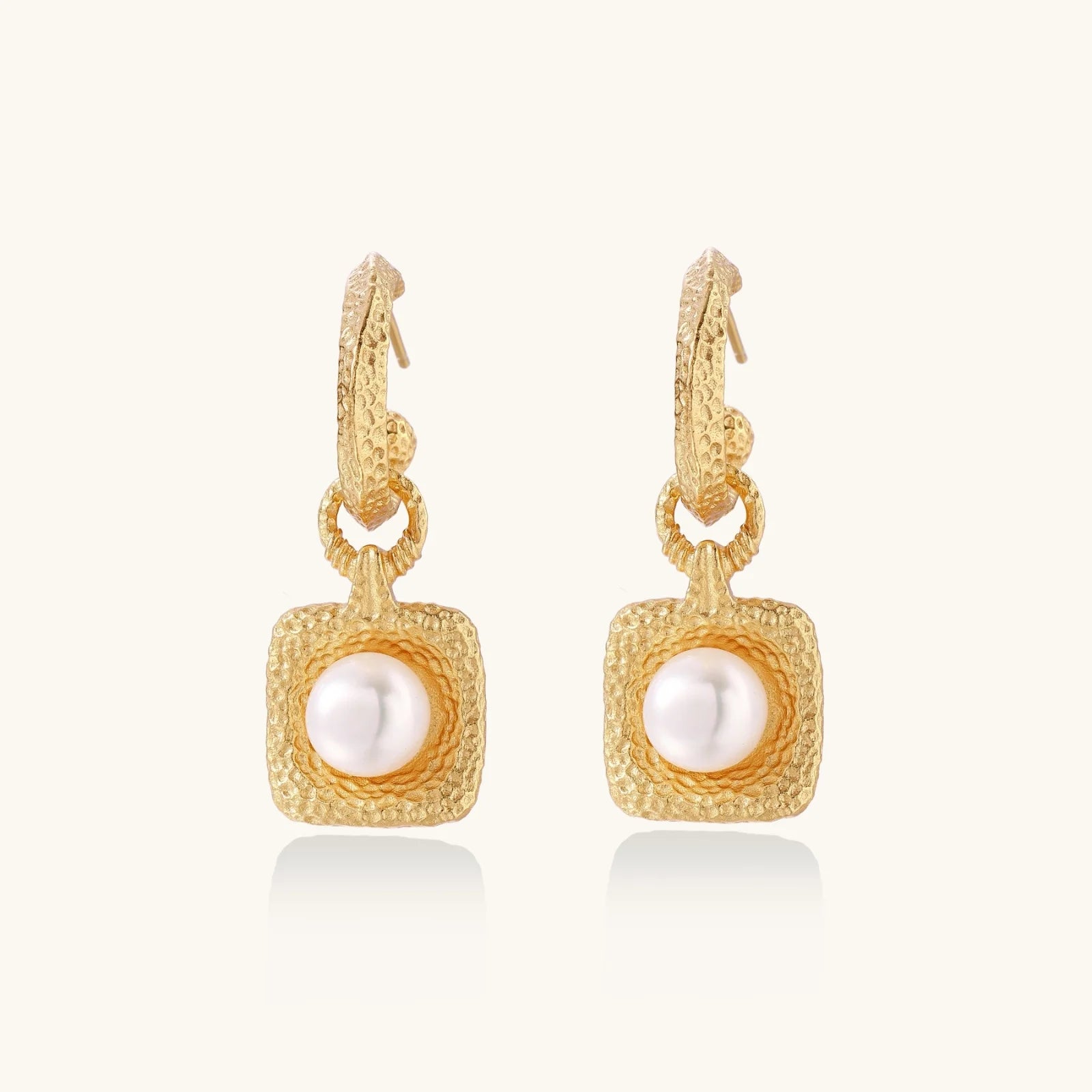 Pair of gold vermeil hoop earrings with textured square frames holding freshwater pearls on cream background