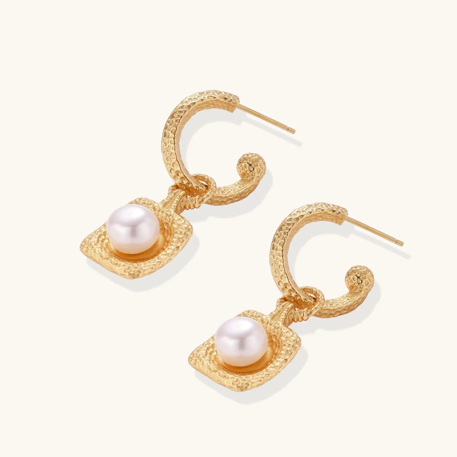 Pair of gold vermeil hoop earrings with textured square frames holding freshwater pearls on cream background