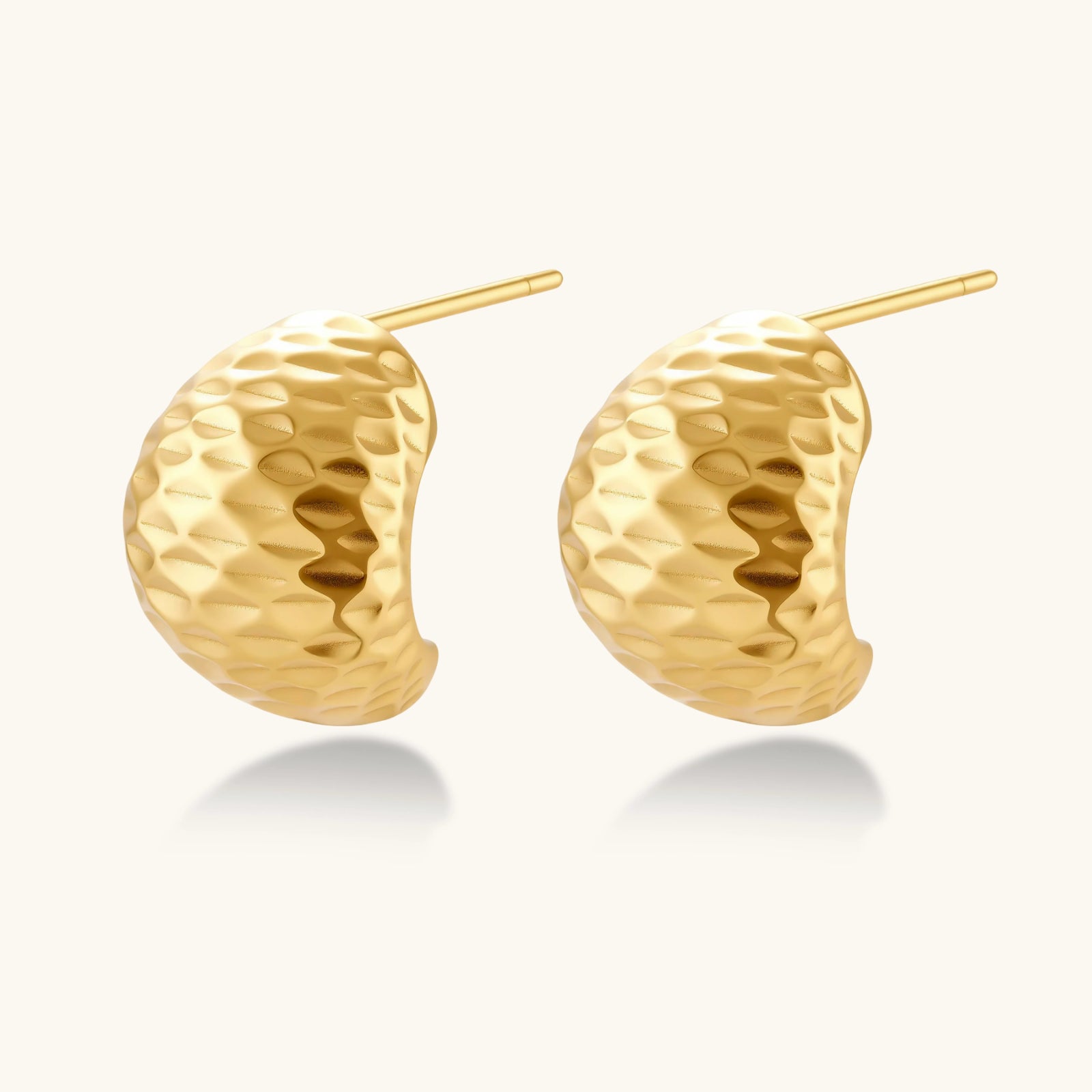 Pair of textured gold-plated sterling silver huggie earrings with dimpled surface finish on cream background.