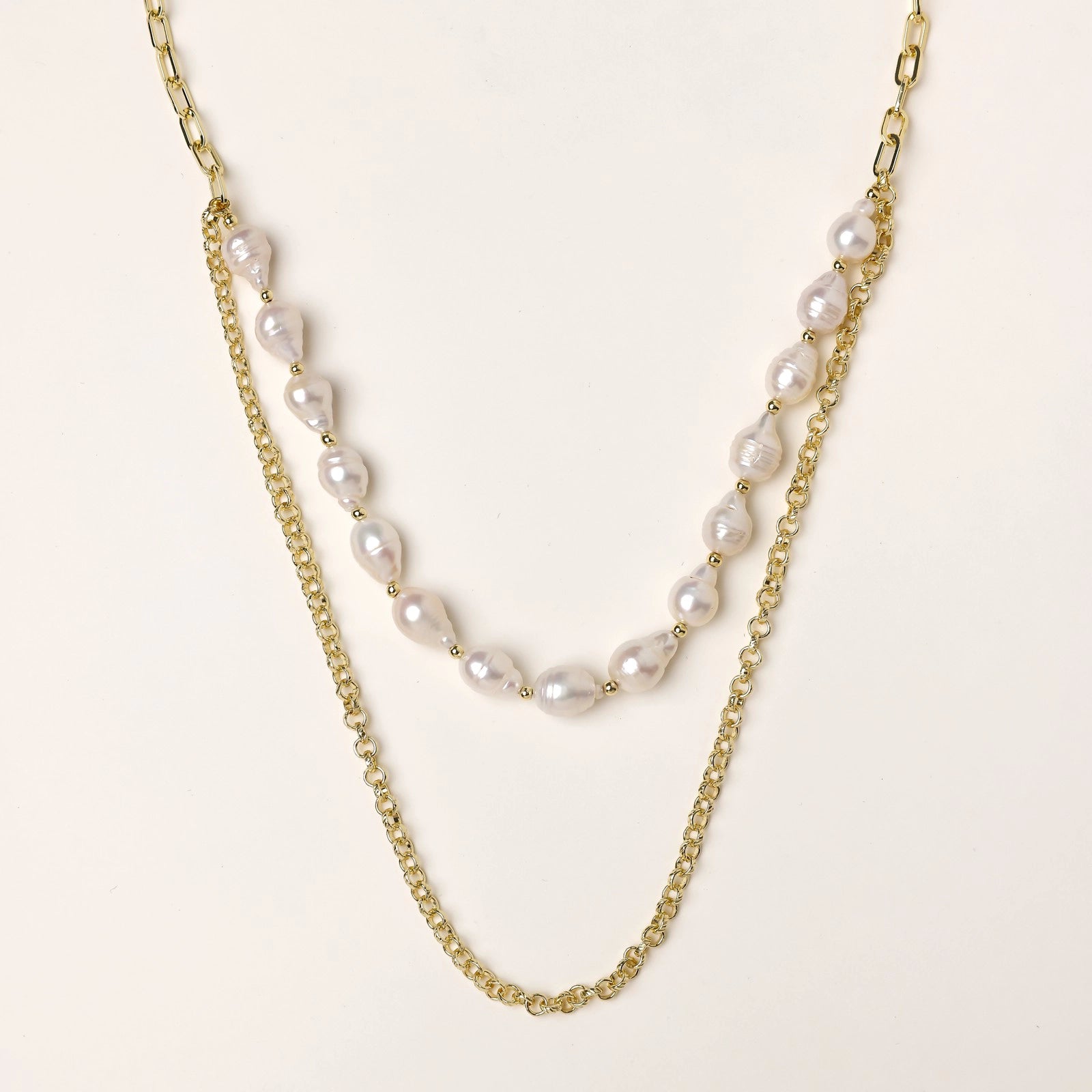 Layered gold chain necklace with organic baroque freshwater pearls and adjustable length on cream background