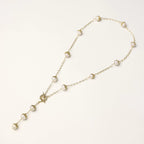 Gold-plated lariat necklace with baroque pearls and textured caps on cream background, showing adjustable Y-shaped design.