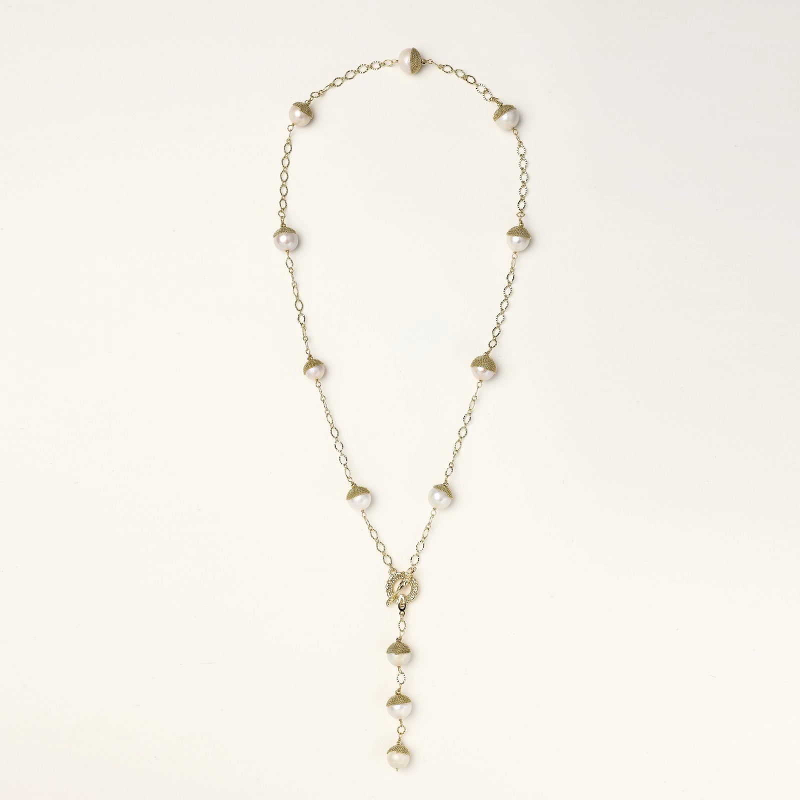Gold-plated lariat necklace with baroque pearls and textured caps on cream background, showing adjustable Y-shaped design.
