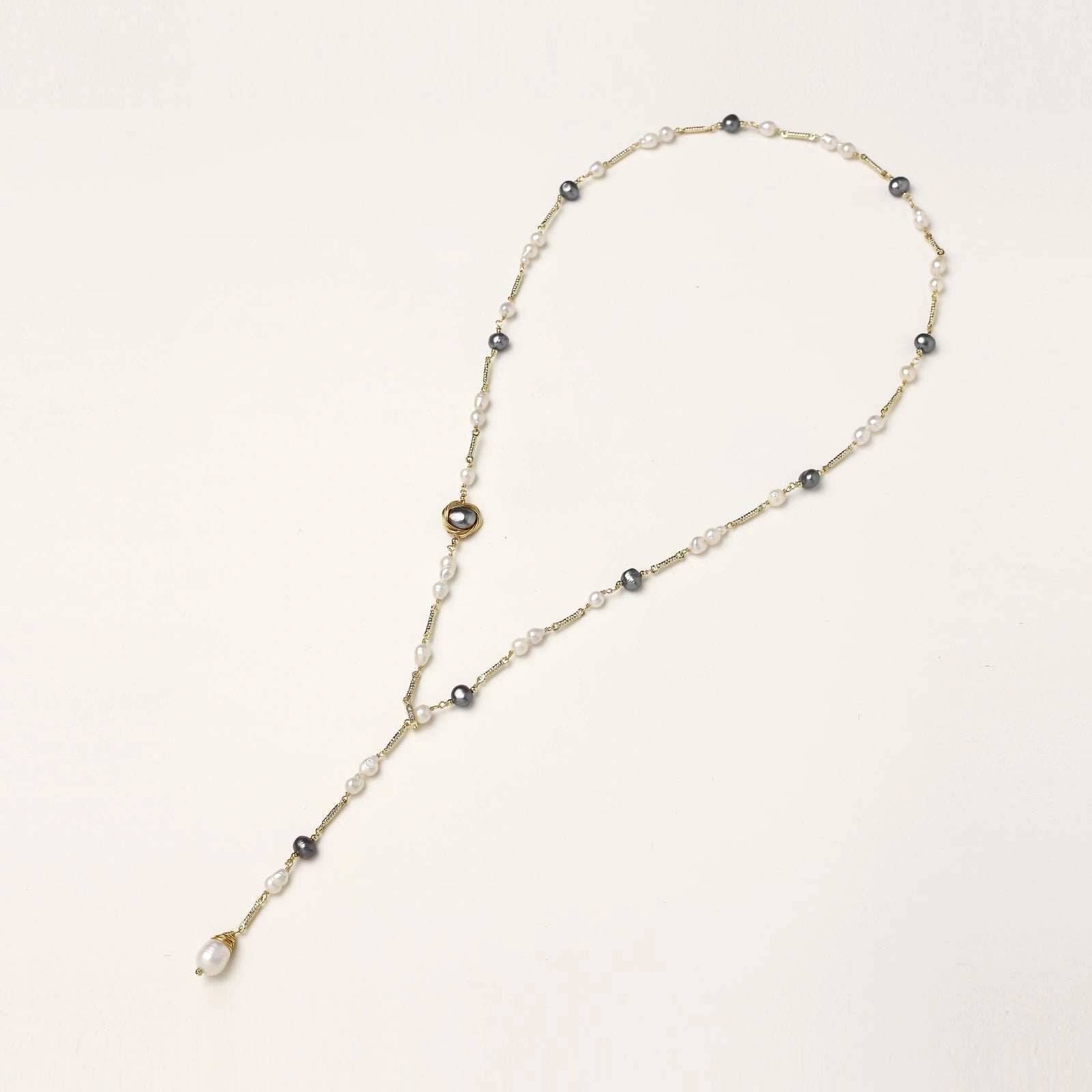 Y-shaped gold-plated necklace with white and gray freshwater pearls on cream background, showing adjustable drop design.