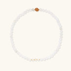Three layered white beaded bracelets with carved orange agate lotus centerpiece and freshwater pearls on cream background.