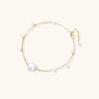 Delicate gold chain bracelet with baroque pearl centerpiece and small freshwater pearls on cream background.