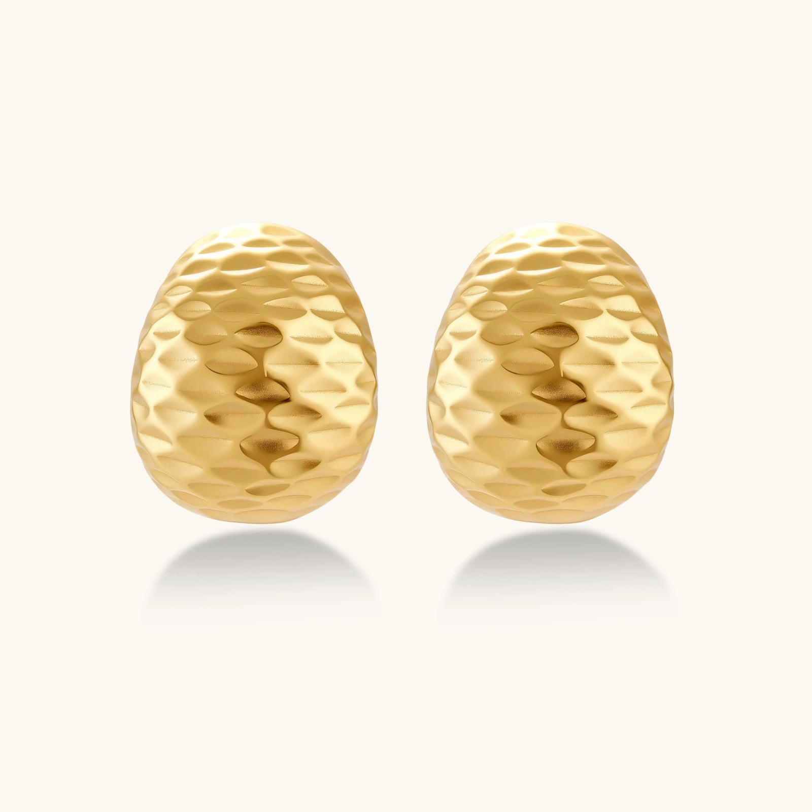 Pair of textured gold-plated sterling silver huggie earrings with dimpled surface finish on cream background.