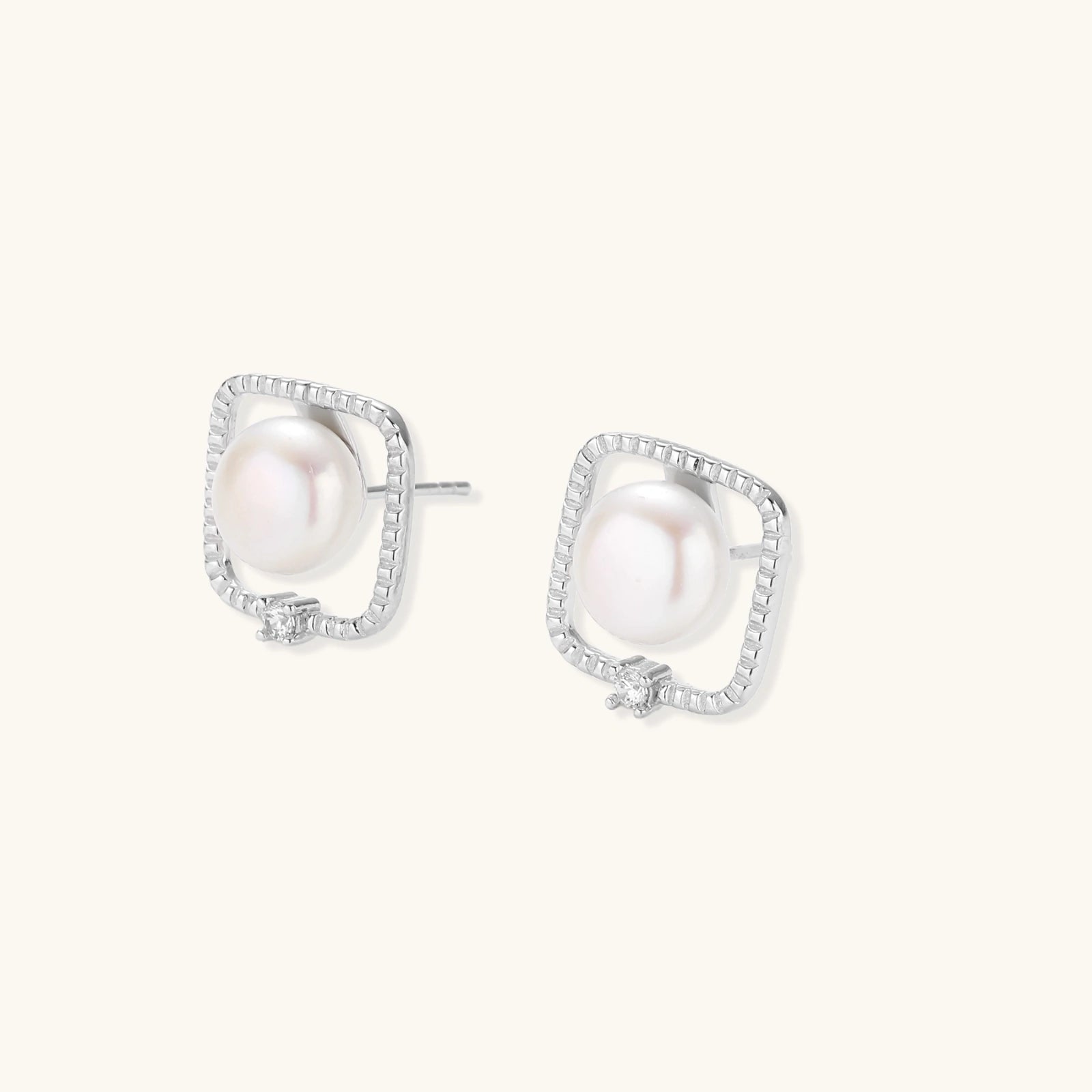 Rhodium-plated silver stud earrings with cushion frame, centered freshwater pearl, and tiny crystal accent