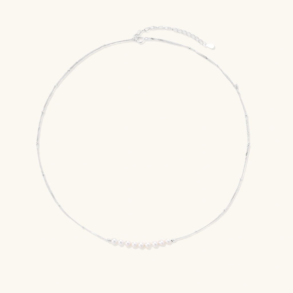 Delicate sterling silver chain necklace with small freshwater pearls arranged in a curved smile arc on cream background.