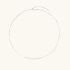 Delicate sterling silver chain necklace with small freshwater pearls arranged in a curved smile arc on cream background.