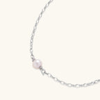Dainty rhodium-plated silver chain necklace with centered 10mm freshwater pearl and crystal accents on cream background