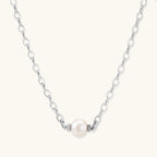 Dainty rhodium-plated silver chain necklace with centered 10mm freshwater pearl and crystal accents on cream background