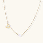 Delicate gold necklace with open heart charm and white pearl bead on fine chain against cream background