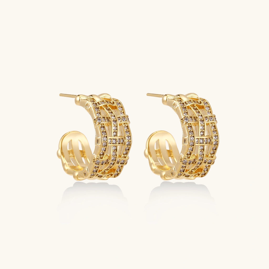 Gold-plated geometric hoop earrings with basket-weave lattice design and pavé crystal accents on cream background