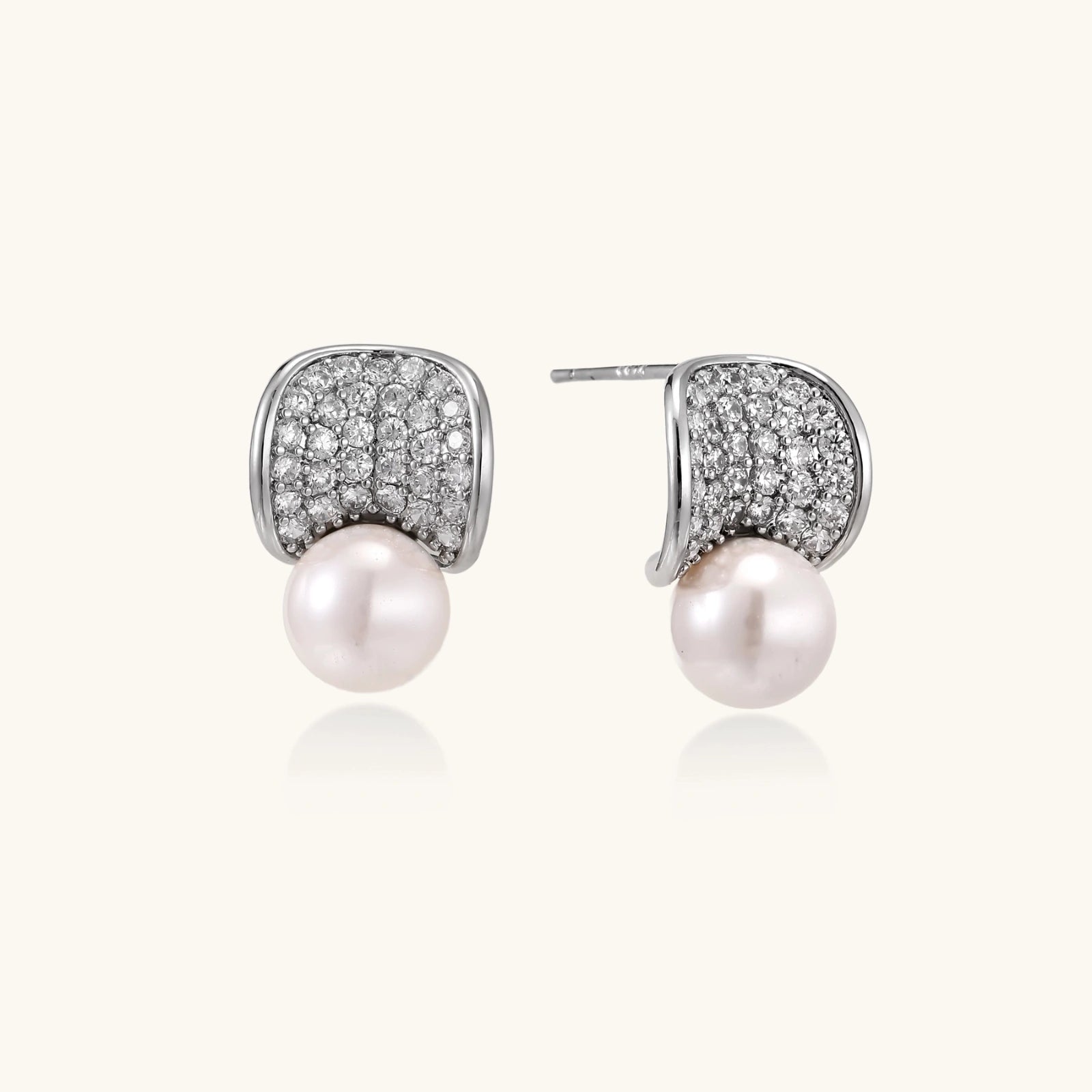 Curved pavé diamond studs in white gold-plated brass cradle lustrous freshwater pearls against cream background