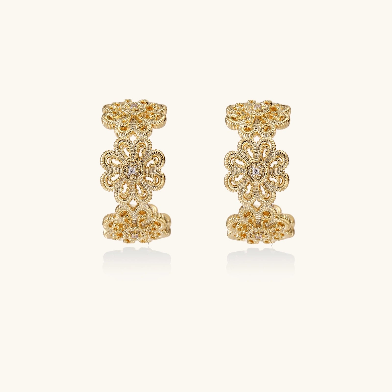 Gold hoop earrings with intricate three-dimensional floral filigree pattern in 14K gold plated brass on cream background
