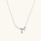 Delicate white gold plated necklace with freshwater pearls and sparkly crystal bow pendant on white background