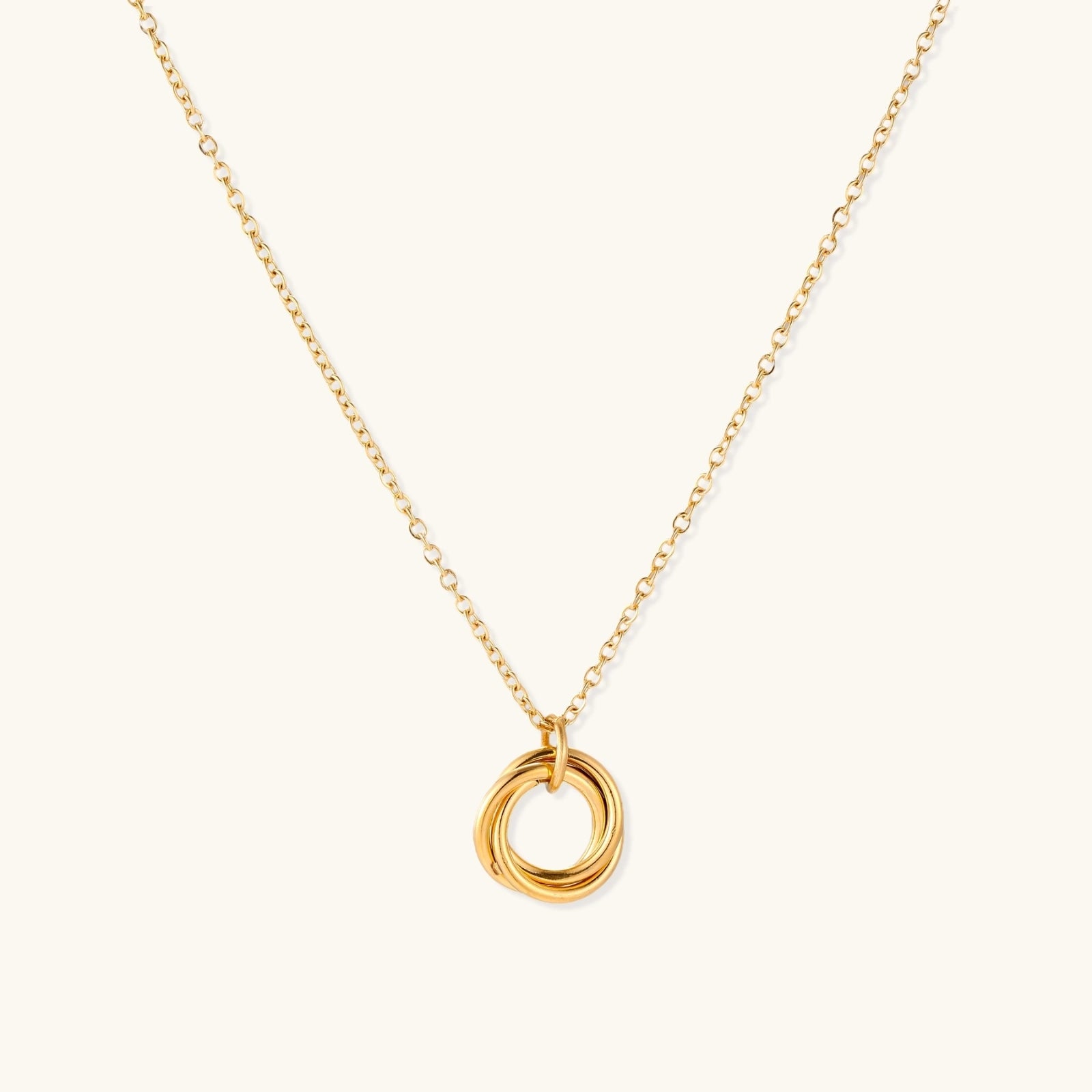 Delicate gold-plated necklace with three interlocking circle rings forming a minimalist knot pendant on cream background