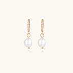 Gold huggie hoop earrings with pavé crystals and white freshwater pearl drops on cream background