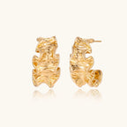 Pair of gold huggie hoops with sculpted wave texture and dimensional ripples on neutral background.