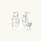 White gold plated sculptural hoop earrings with organic wavy edges and reflective metallic finish on cream background