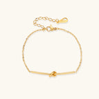 Delicate gold chain bracelet with minimalist bar and centered knot detail on cream background