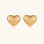 Gold heart-shaped stud earrings with parallel ridged texture on cream background