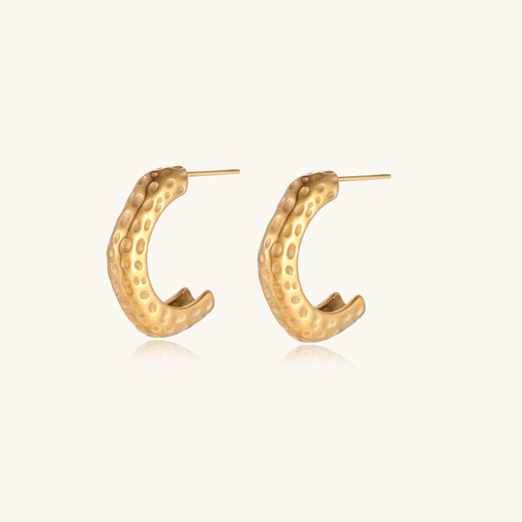Gold-toned hoop earrings with hammered dimpled texture and post closure on cream background