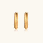 Chunky tubular hoop earrings in warm 14K gold-plated finish with smooth polished surface on cream background.