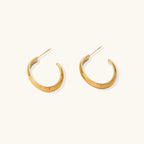 Chunky tubular hoop earrings in warm 14K gold-plated finish with smooth polished surface on cream background.