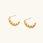Gold-plated chunky hoop earrings with ridged bubble texture on cream background